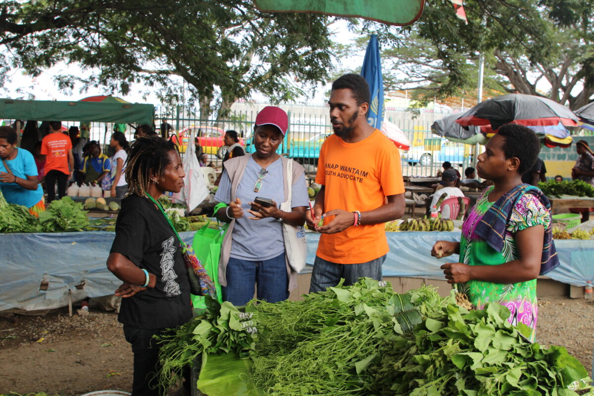 Jamie Wartovo, Sanap Wantaim male youth advocate, and Jacinta Kasozi, International United Nations volunteer engaging in discussion with a market vendor